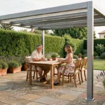Couple installé sous une pergola aluminium 4x3 sur une terrasse en pierre avec jardin verdoyant en arrière-plan