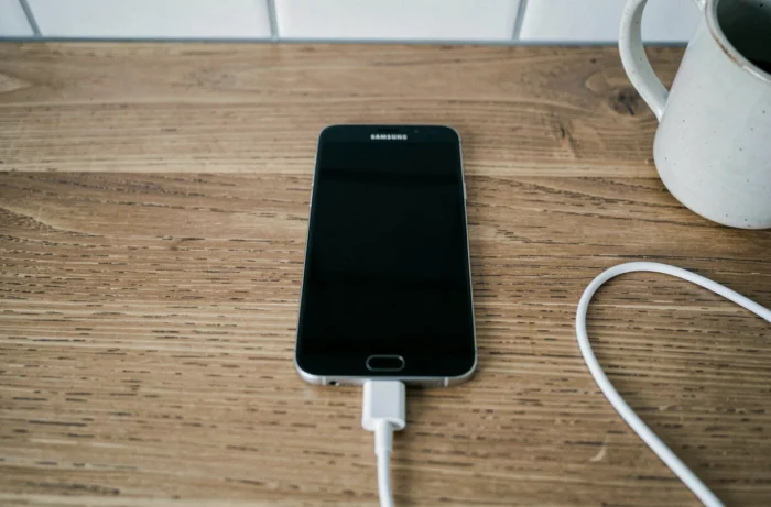 Samsung Galaxy avec écran noir branché sur chargeur posé sur une table en bois lors d'un diagnostic