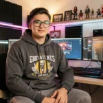 Jeune YouTubeur masculin assis devant son setup gaming et streaming dans un home studio moderne avec moniteurs et panneaux acoustiques